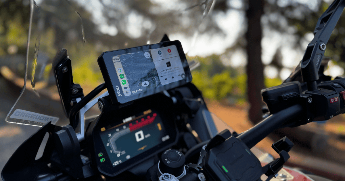 Navigatore per moto JADO con CarPlay montato sul manubrio di una maxi enduro, davanti alla strumentazione TFT, in controluce